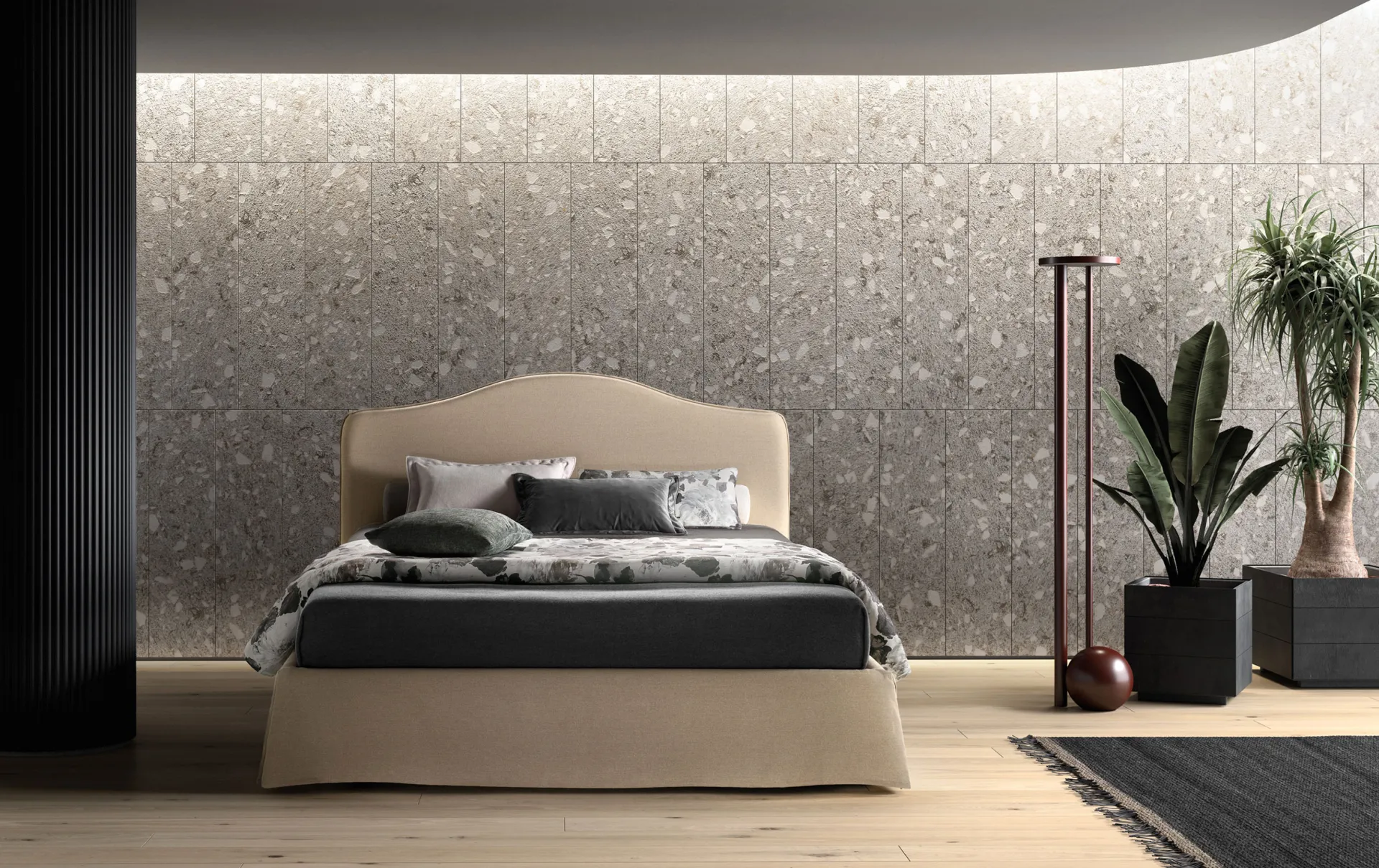 Letto imbottito Lovely Samoa beige con testiera sagomata e balza fino a terra, davanti a una parete in graniglia