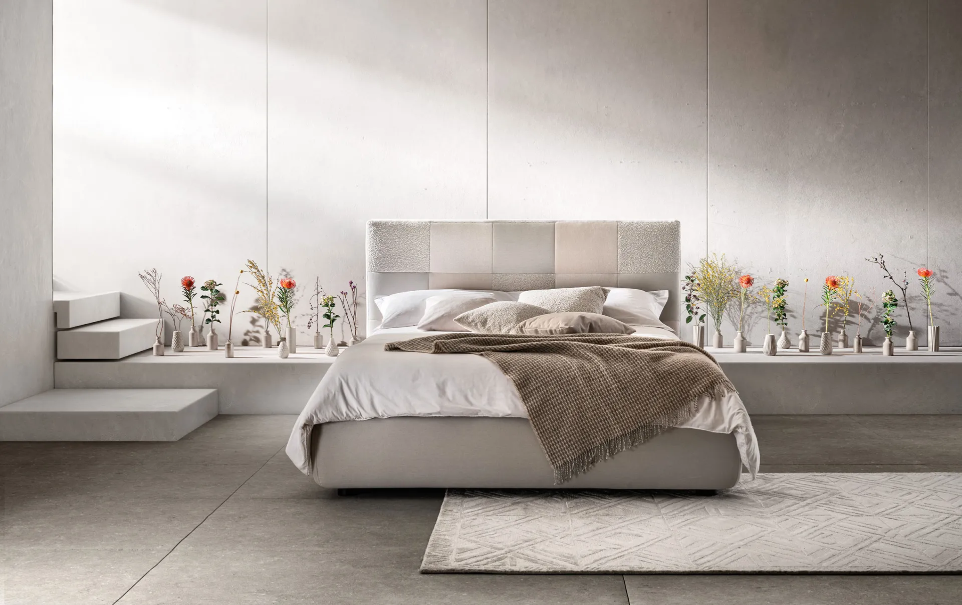 Letto imbottito Essential Samoa panna con testiera a riquadri, davanti a una mensola con fiori