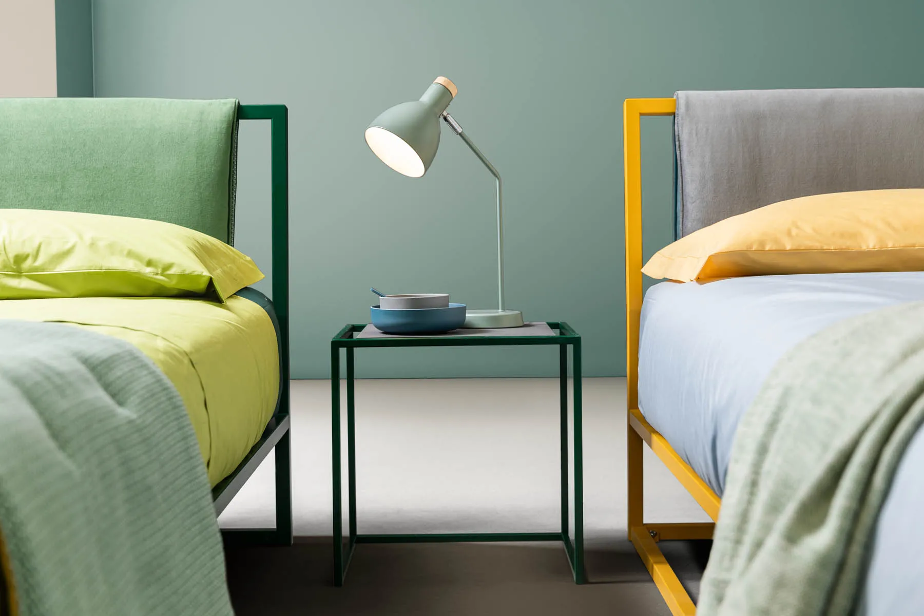 Tavolino Frame Samoa a telaio verde fra due letti imbottiti con testiere in metallo colorato