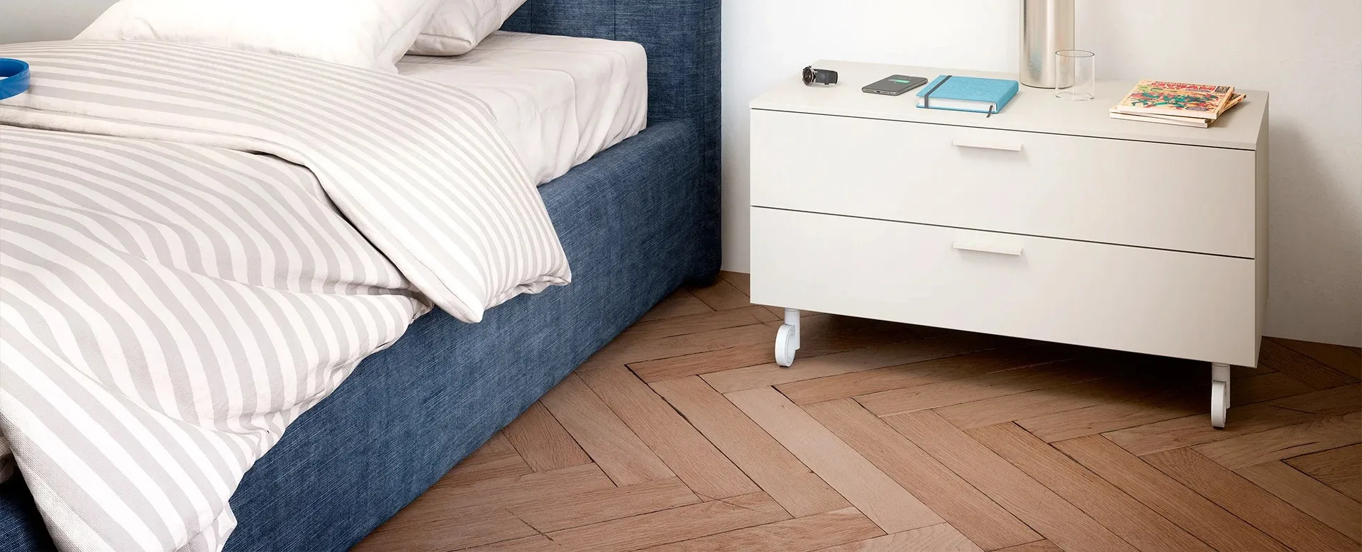 Comodino con ruote Nidi bianco a due cassetti accanto al letto blu