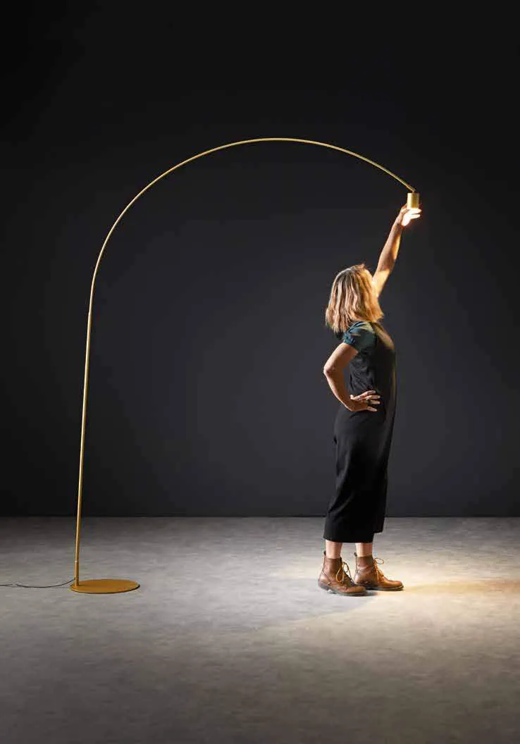 Piantana ad arco Maison Fan Europe oro in una stanza scura con una donna