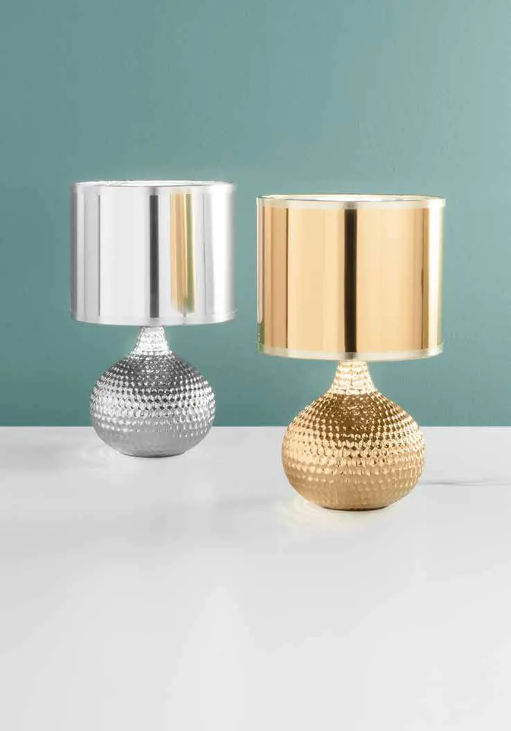 Lampade da tavolo Pulsar Fan Europe silver e oro davanti a una parete verde