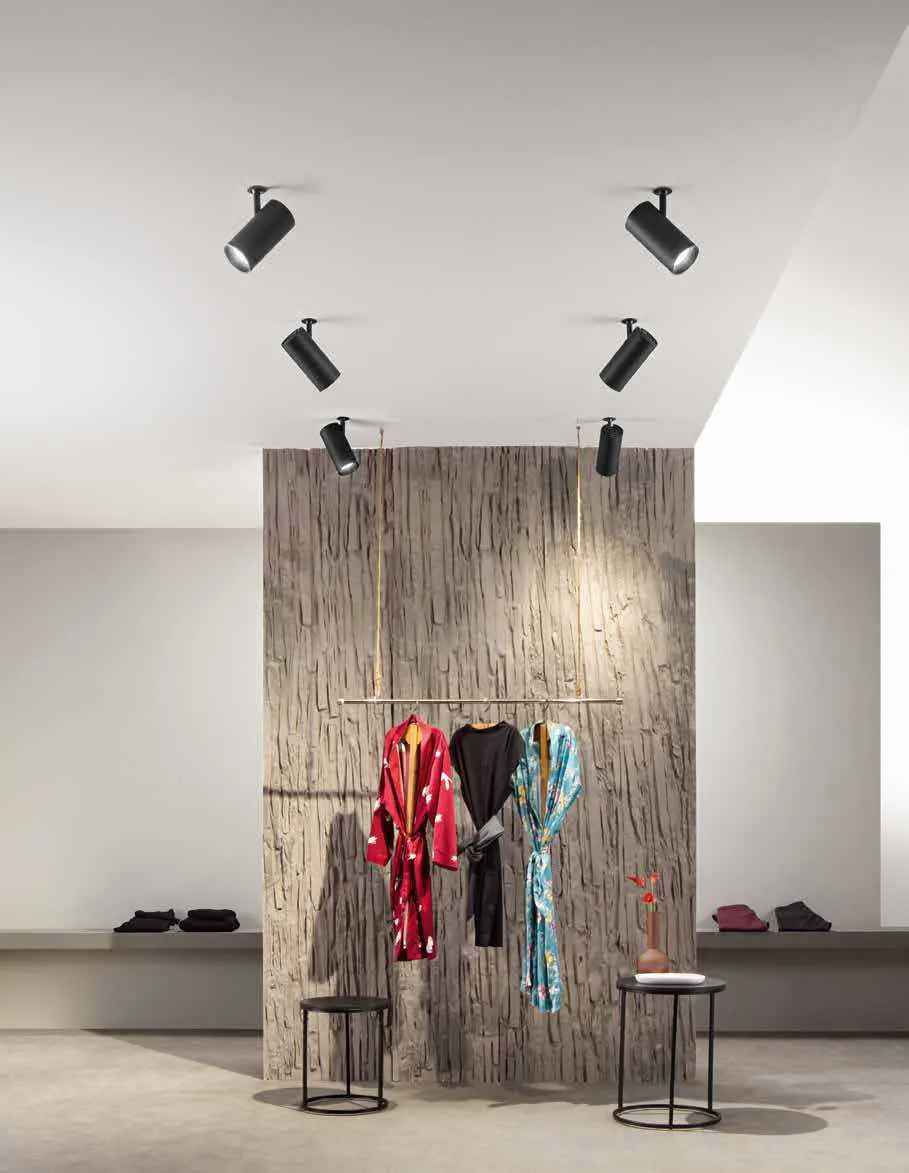 Faretti Shift Spot Fan Europe neri sopra una parete in legno con abiti esposti