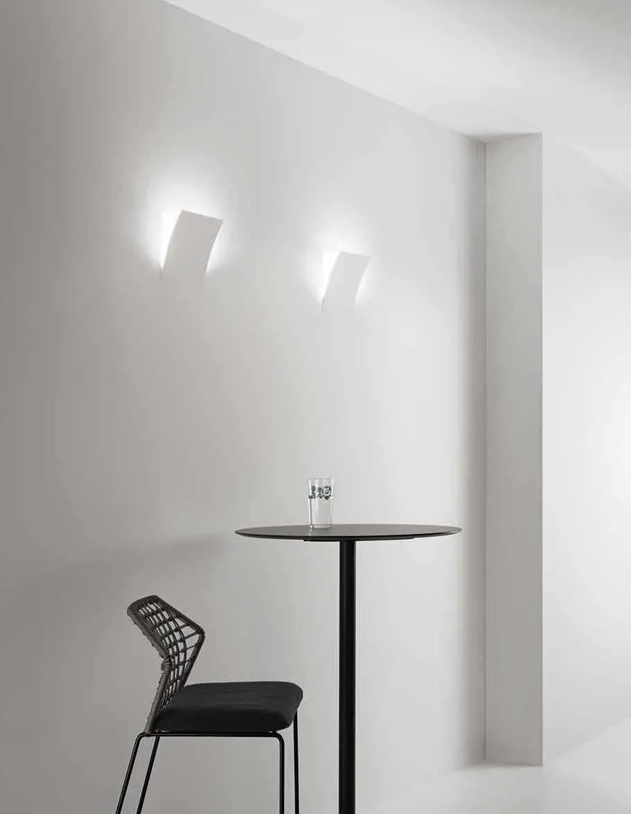Applique in gesso Anima Fan Europe accese su una parete bianca accanto a un tavolino alto