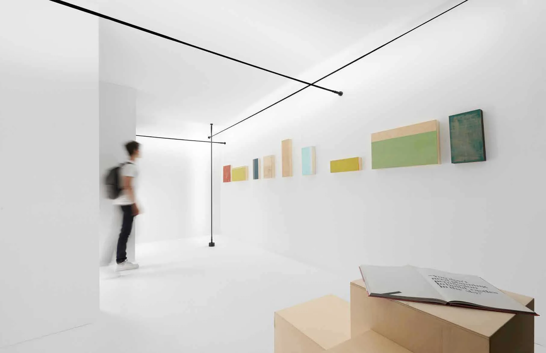 Linee di luce Segmento Fan Europe nere tese fra parete e soffitto in una galleria bianca