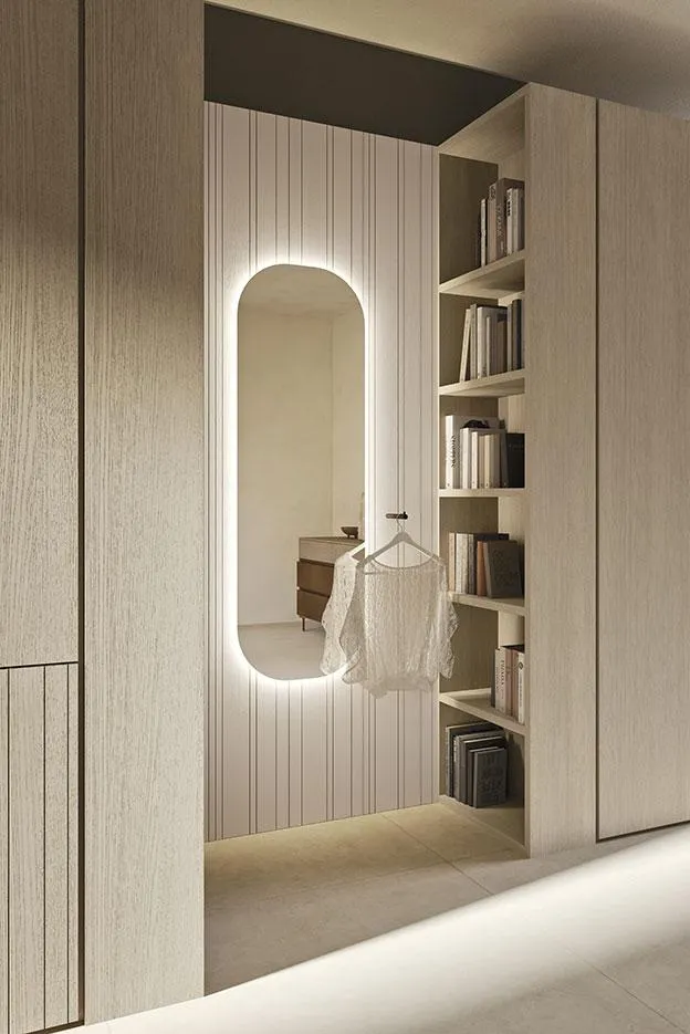 Specchio ovale illuminato Oval MobilGam accanto a una libreria