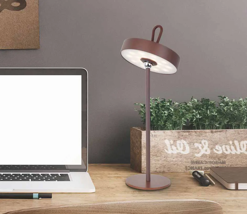 Lampada portatile Gong Schuller color corten su una scrivania accanto a un portatile