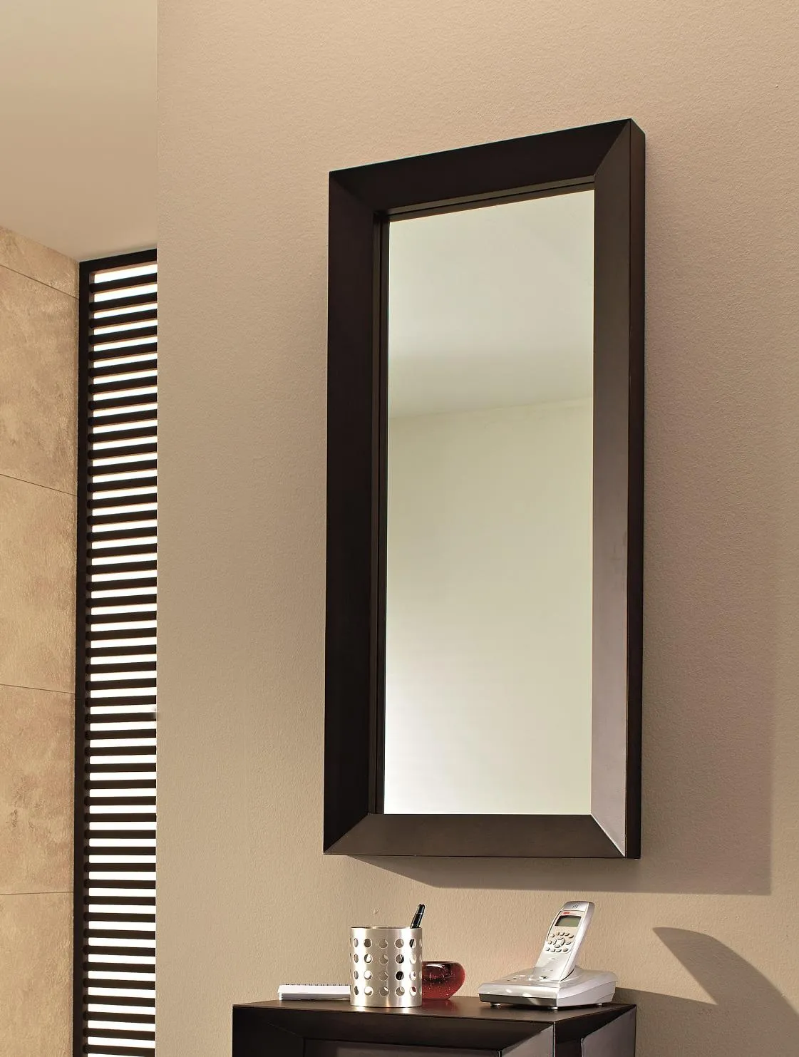Specchio EL/006 Stones con cornice scura appeso sopra un mobile basso in un ingresso