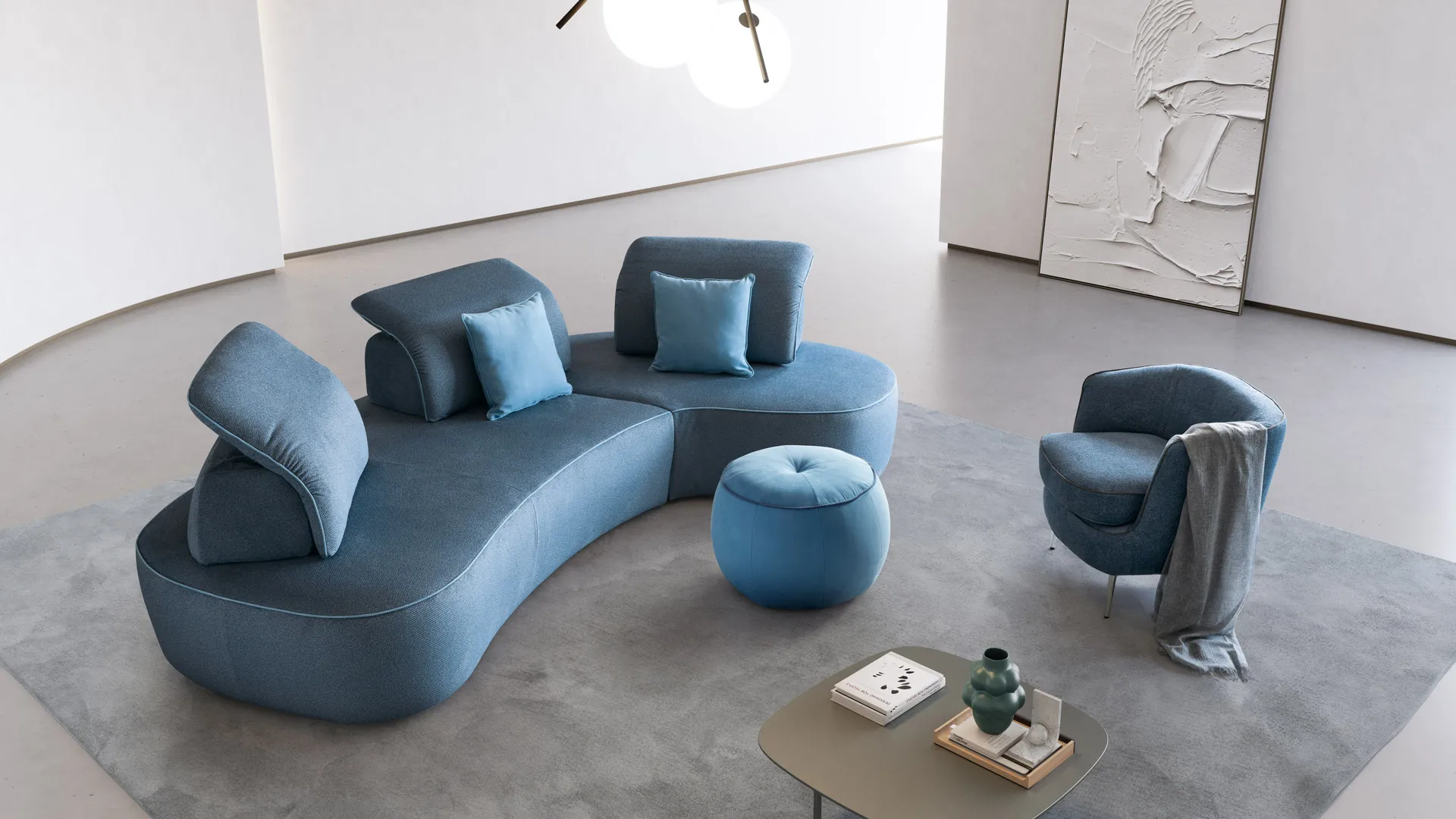 Divano curvo Bean Aerre Divani blu con pouf rotondo e poltrona in un soggiorno grigio