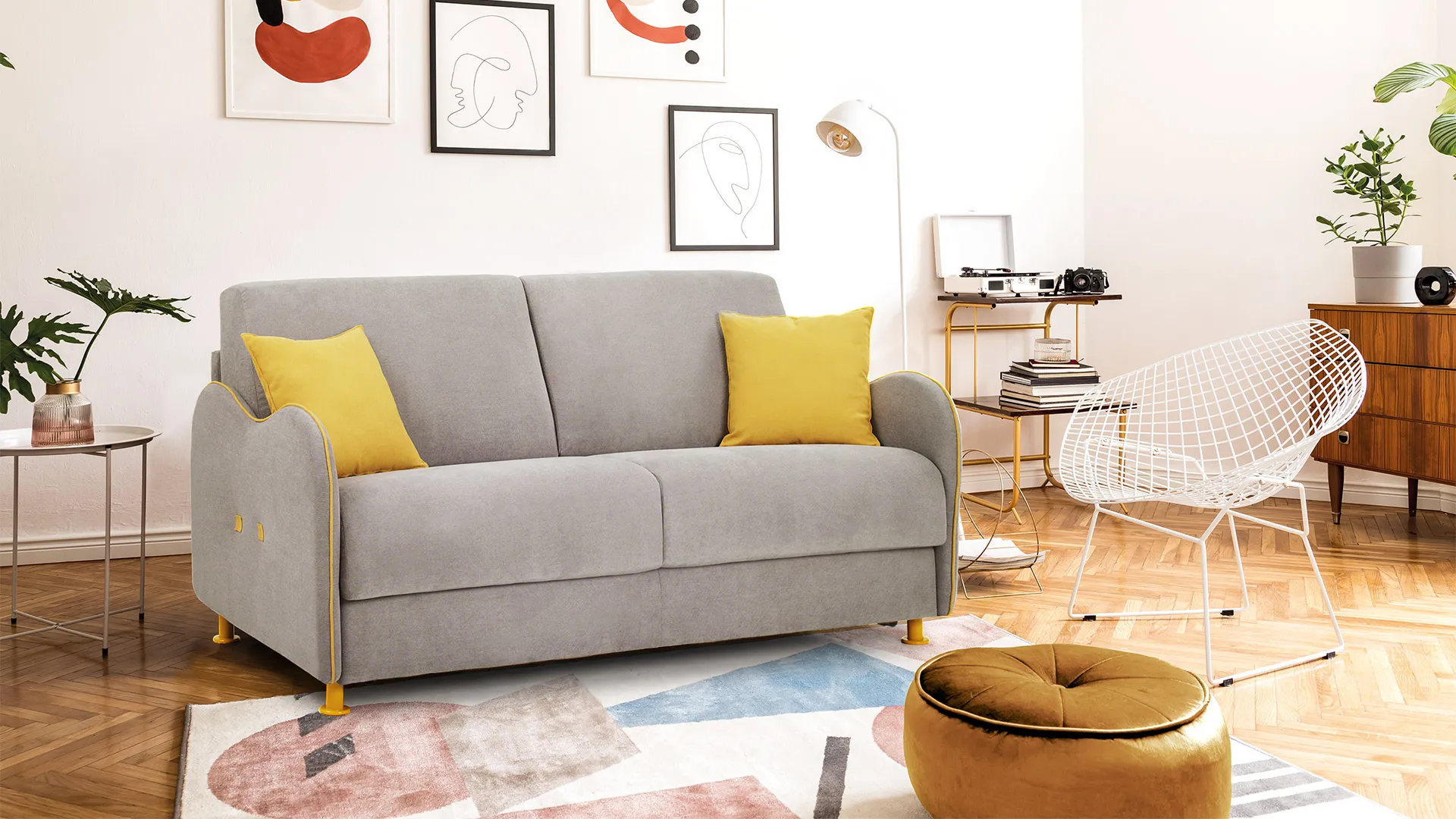Divano letto Titti Basic Aerre Divani grigio con cuscini gialli in un soggiorno con pouf ocra e quadri