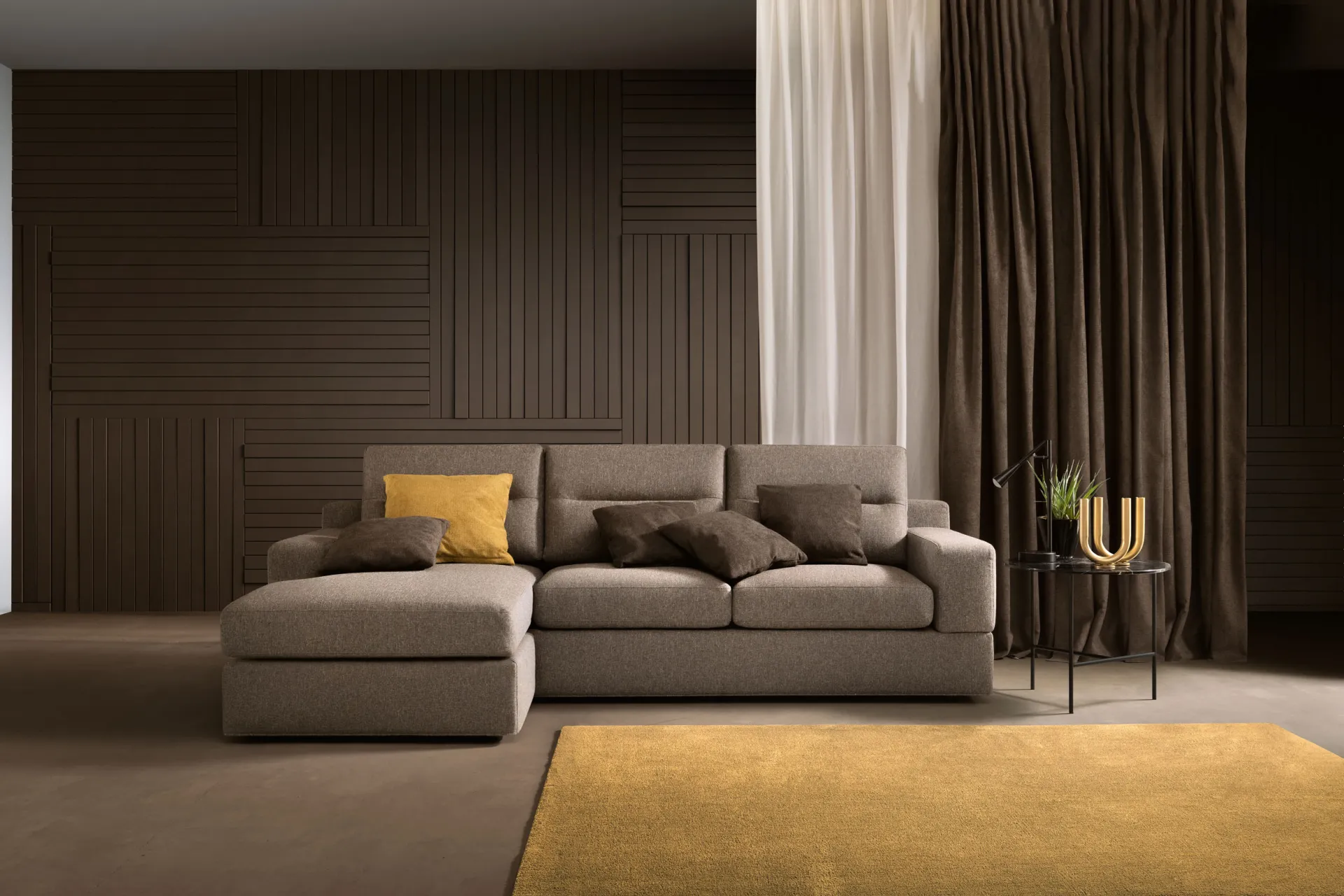 Divano Newport Samoa grigio tortora con chaise longue e base a terra, su tappeto giallo