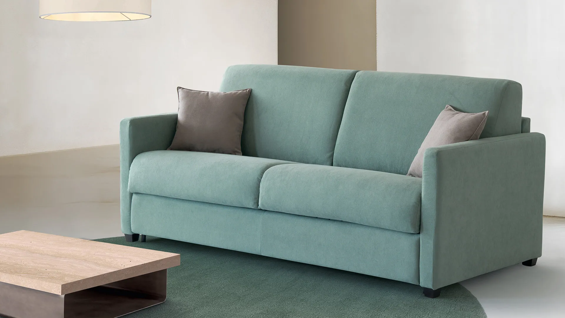 Divano letto Corinne Aerre Divani verde acqua con tavolino basso in legno su tappeto