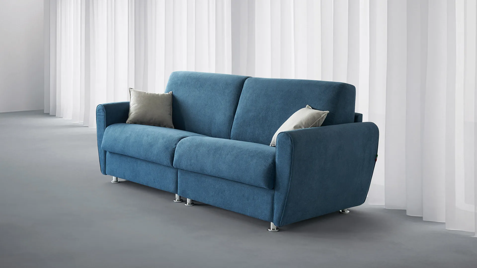 Divano doppio letto Gina Basic Aerre Divani blu con cuscini beige in una stanza con tende bianche