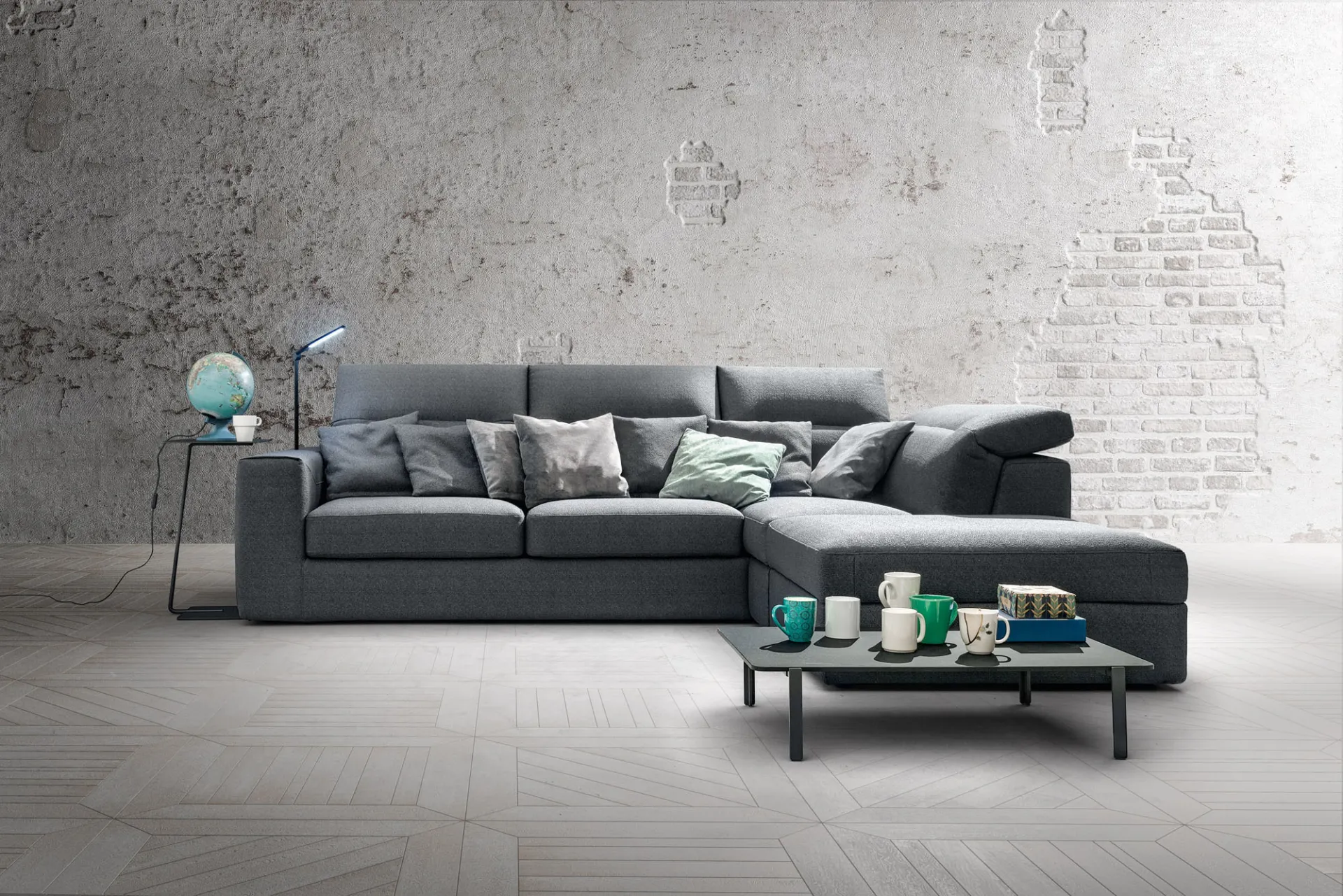 Divano Zippy Samoa grigio antracite con penisola e schienali reclinabili, davanti a un muro in mattoni chiari