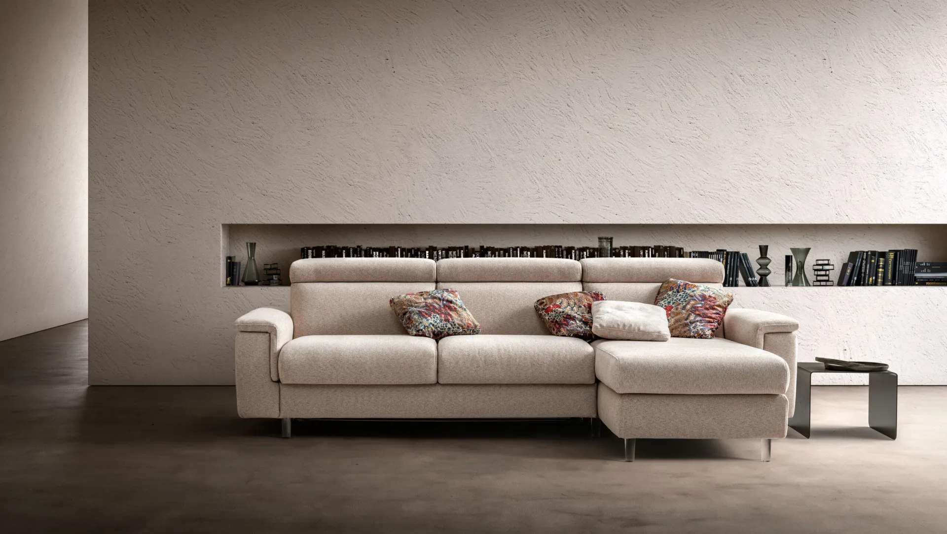 Divano letto Target Samoa beige con chaise longue e poggiatesta, davanti a una nicchia con libri
