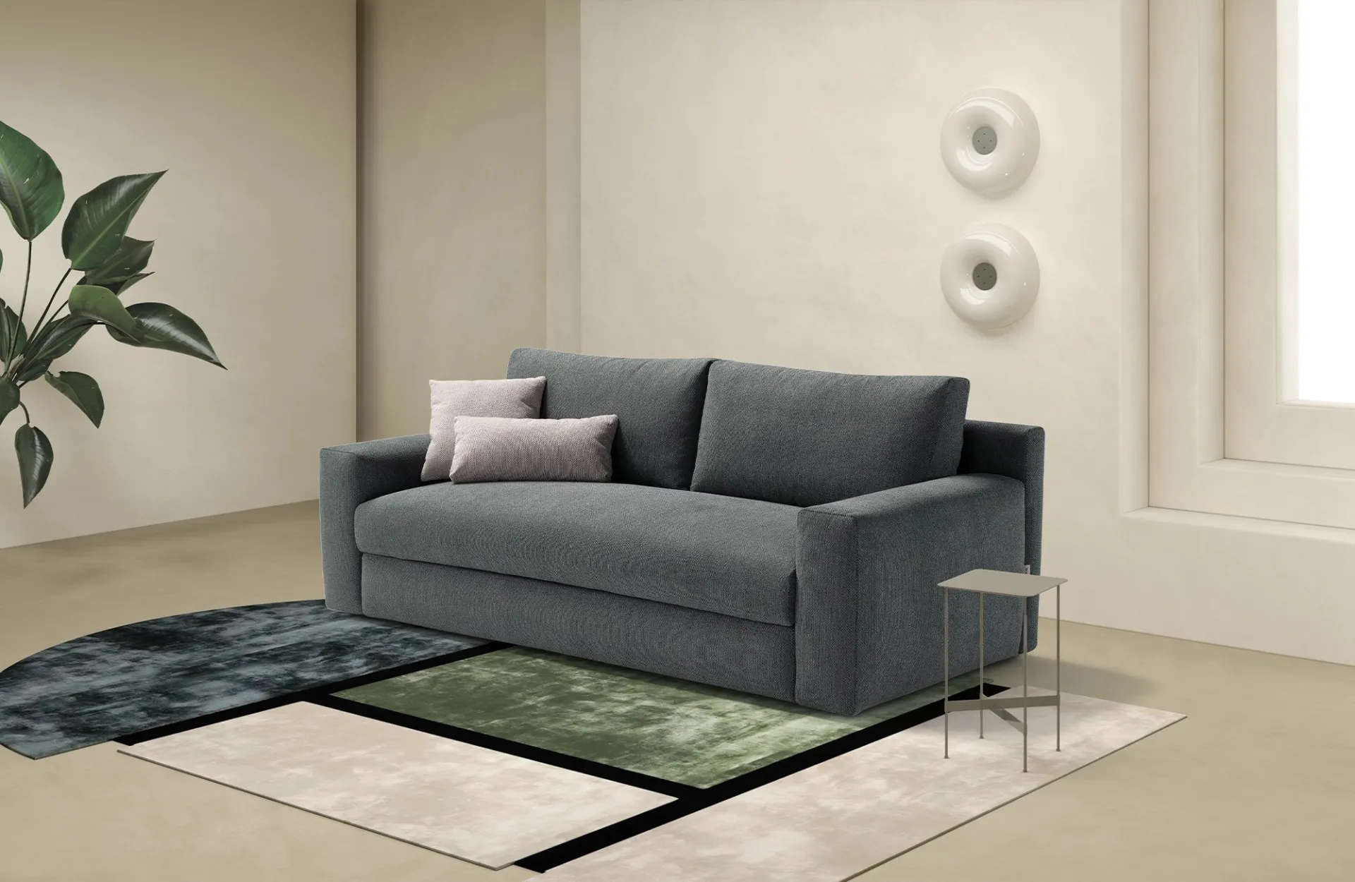 Divano letto Loop Dienne grigio antracite con cuscini rosa cipria in un soggiorno con pianta
