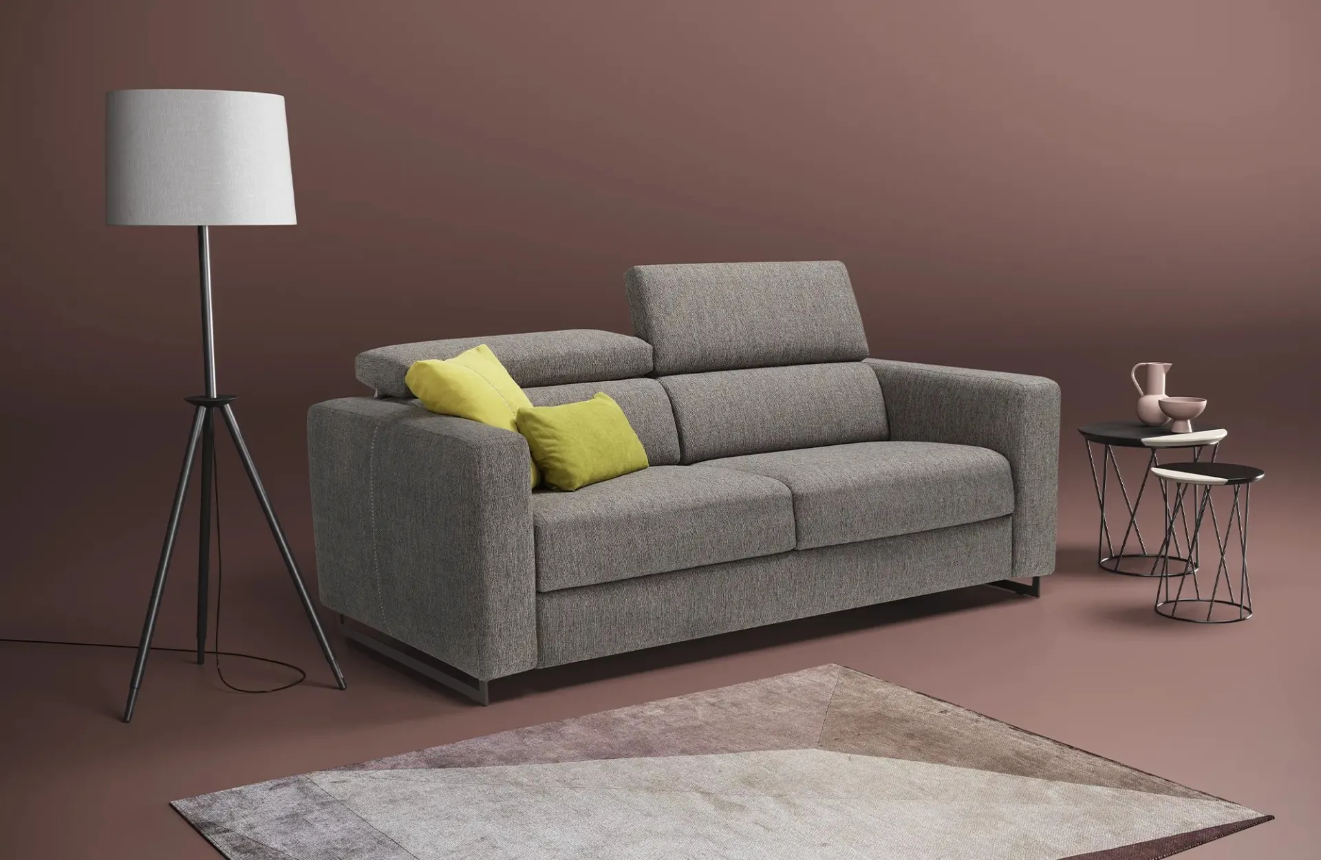 Divano letto Modular Pro Dienne grigio con un poggiatesta alzato, lampada e tavolini in una stanza rosa