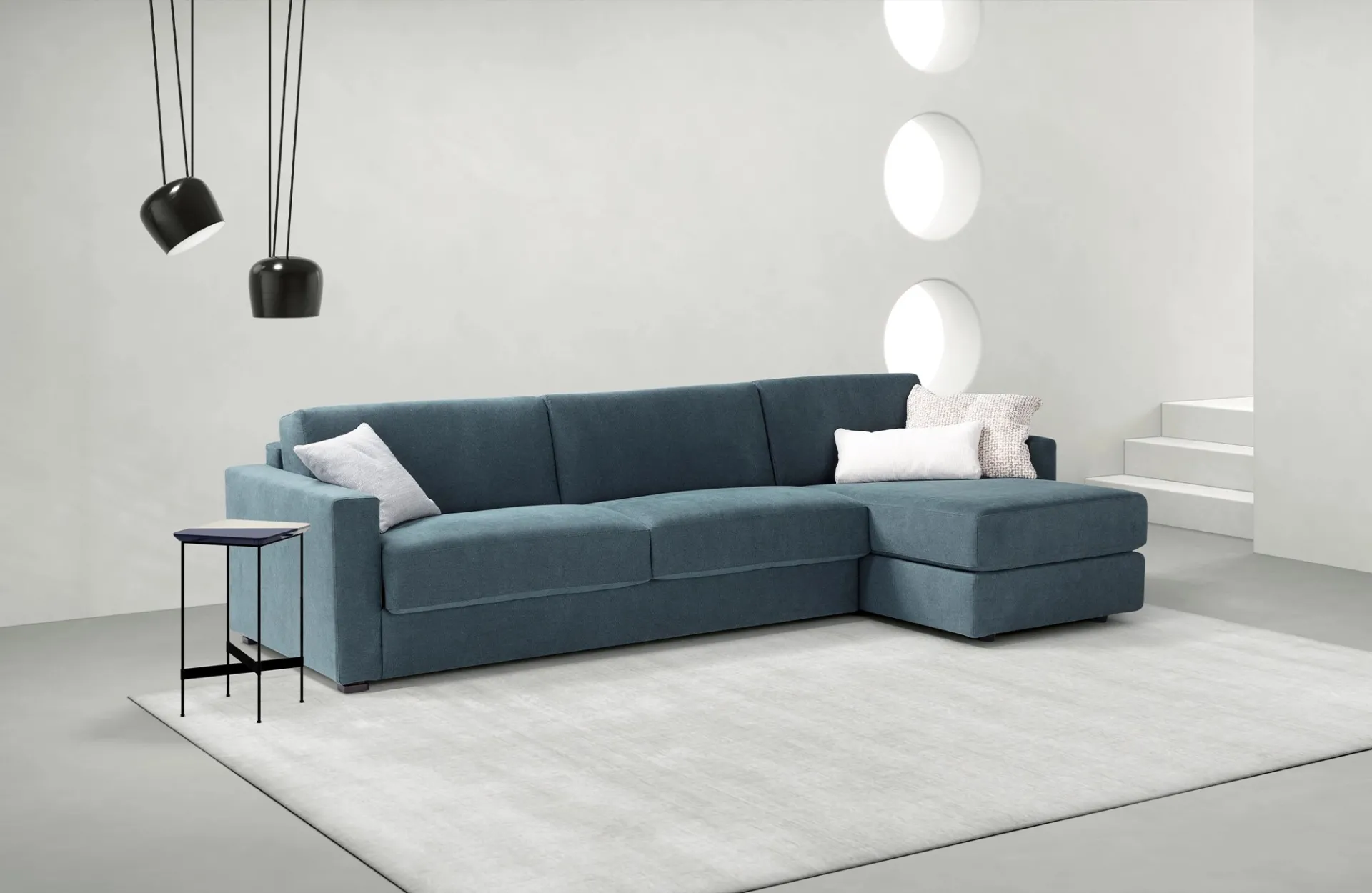 Divano letto Amsterdam Dienne blu petrolio con penisola, sotto due lampade a sospensione nere