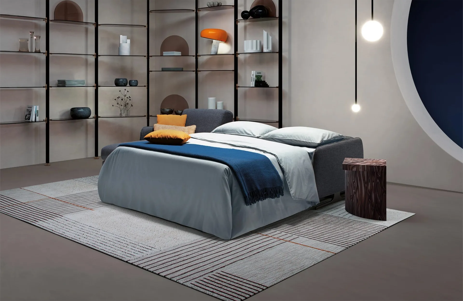 Divano letto Revival Dienne aperto con coperta blu davanti alla libreria