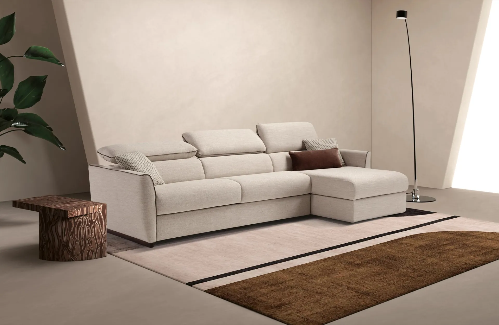 Divano letto Fellini Dienne beige con chaise longue e poggiatesta, accanto a un ceppo in legno