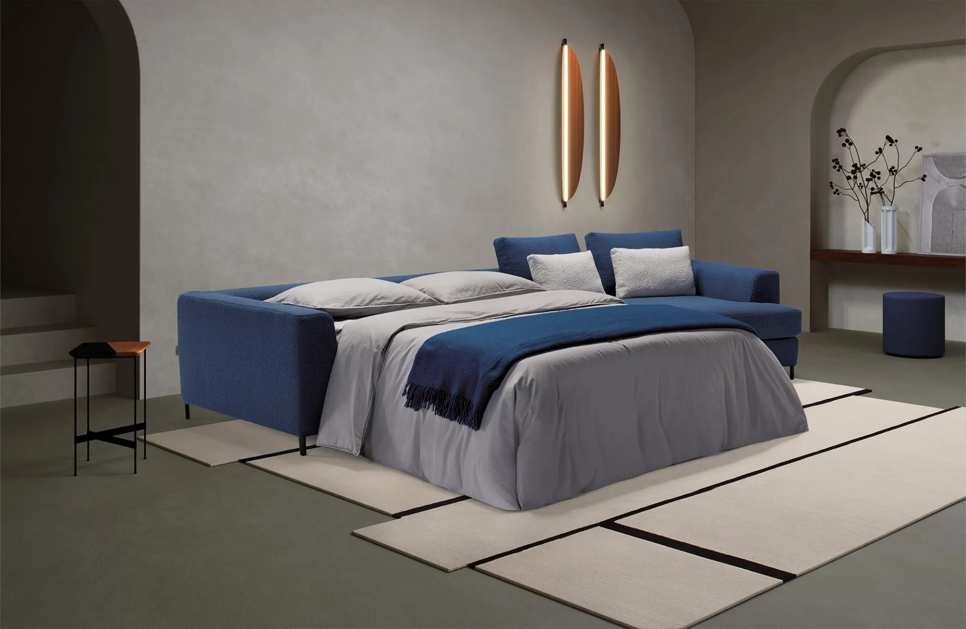 Divano letto Loy Dienne aperto con coperta blu accanto al terminale