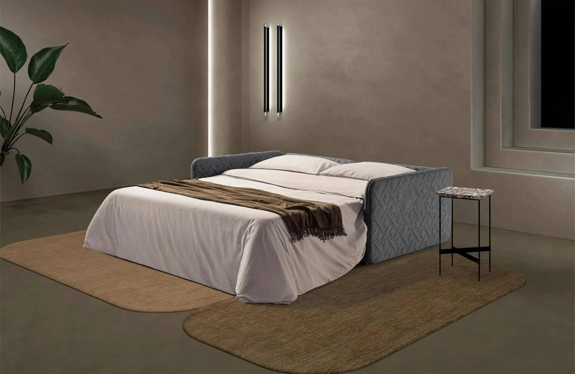 Divano letto Lia Dienne aperto con lenzuola bianche e coperta marrone