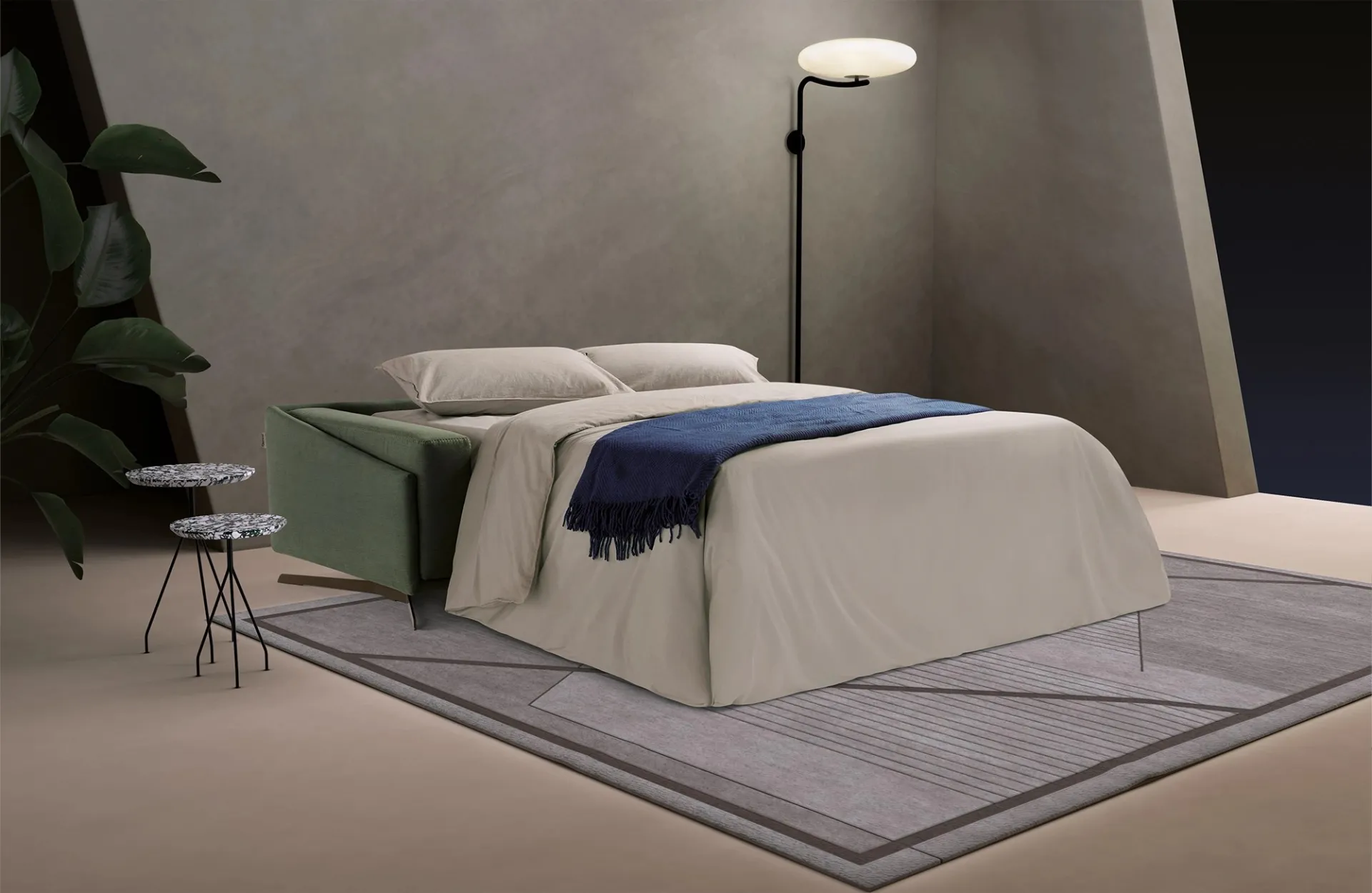 Divano letto Space Dienne aperto con coperta blu sotto una lampada a stelo