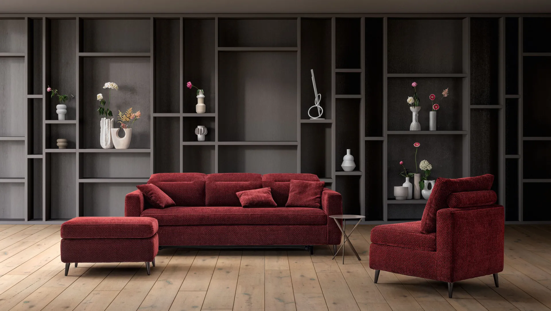 Divano trasformabile Ghost Samoa rosso con pouf e poltroncina, davanti a una libreria scura