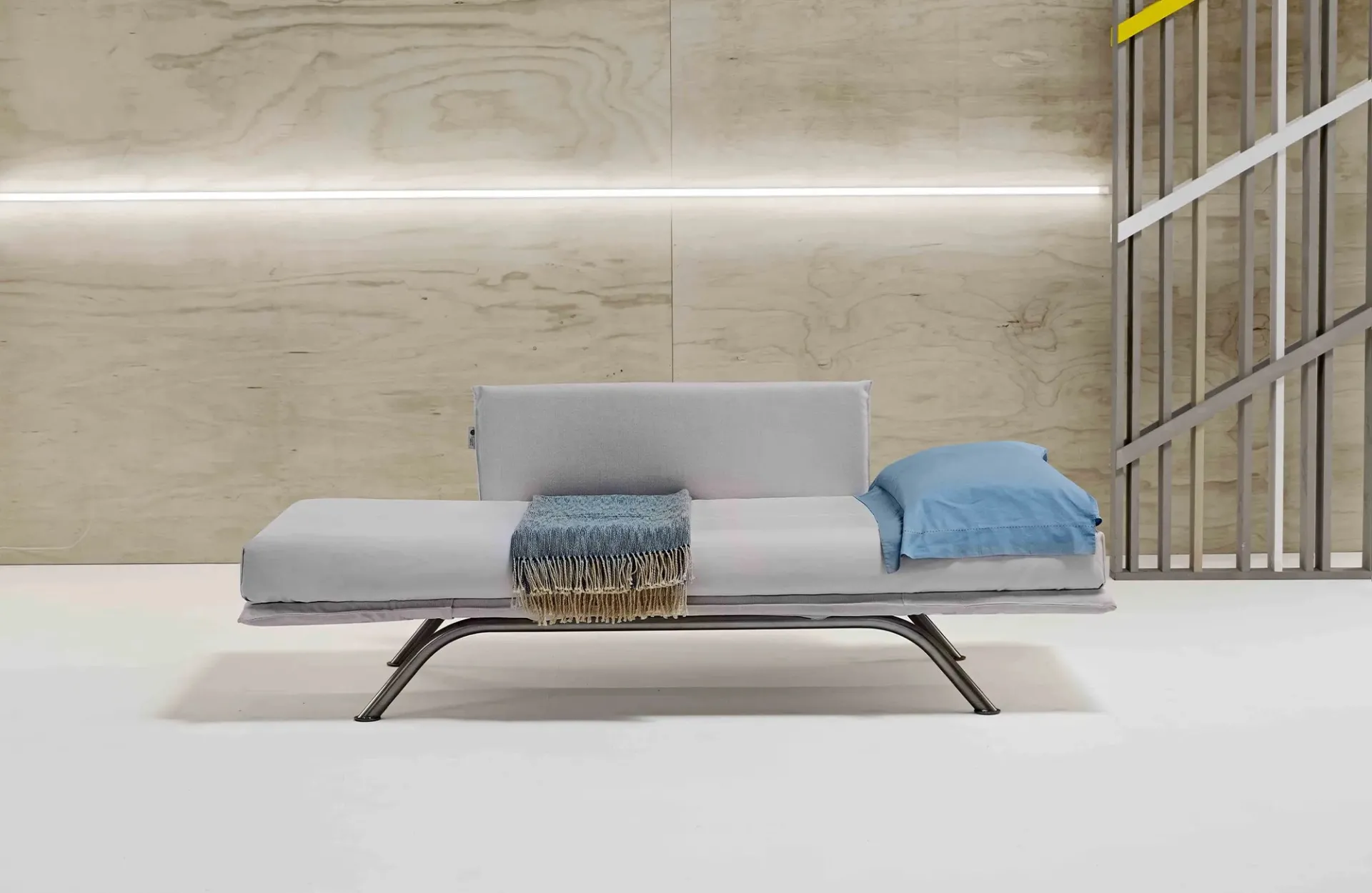 Divano letto Nicla Dienne con i braccioli abbassati, cuscino azzurro e coperta