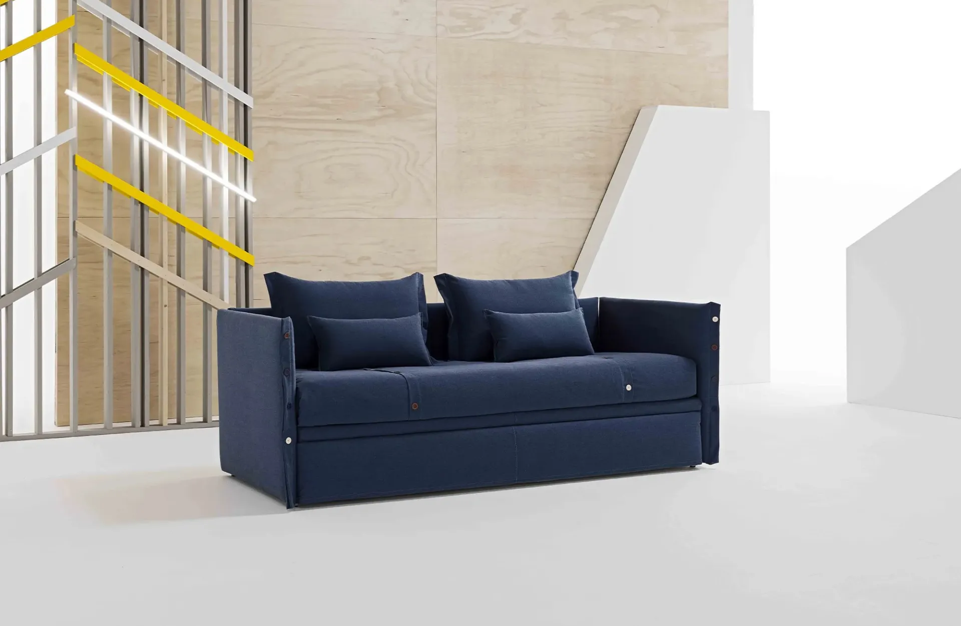 Divano letto Iceberg Dienne blu notte con cuscini di schienale davanti a una parete in legno chiaro