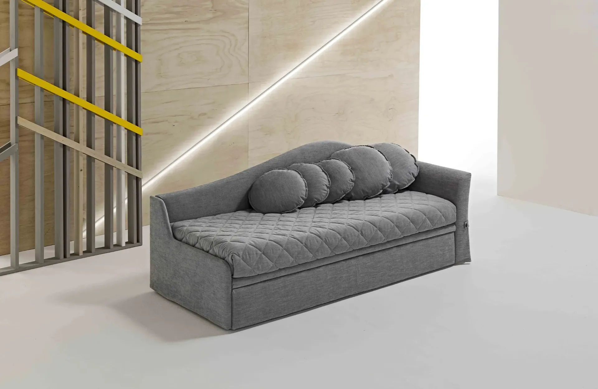 Divano letto Dalila Dienne grigio con schienale a onda e cuscini a rullo in uno spazio luminoso