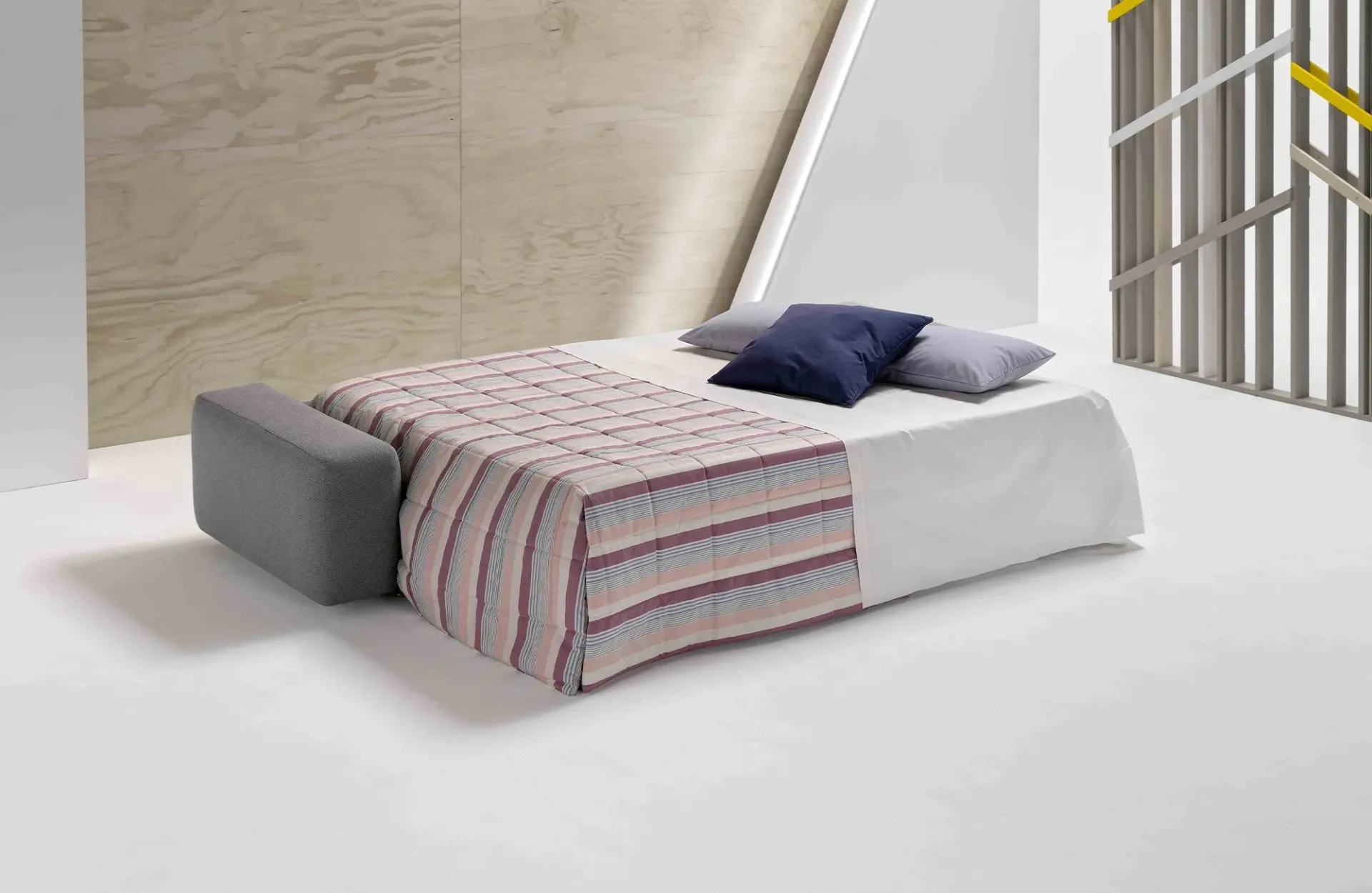 Divano letto Cross Dienne aperto con copriletto a righe e cuscini blu
