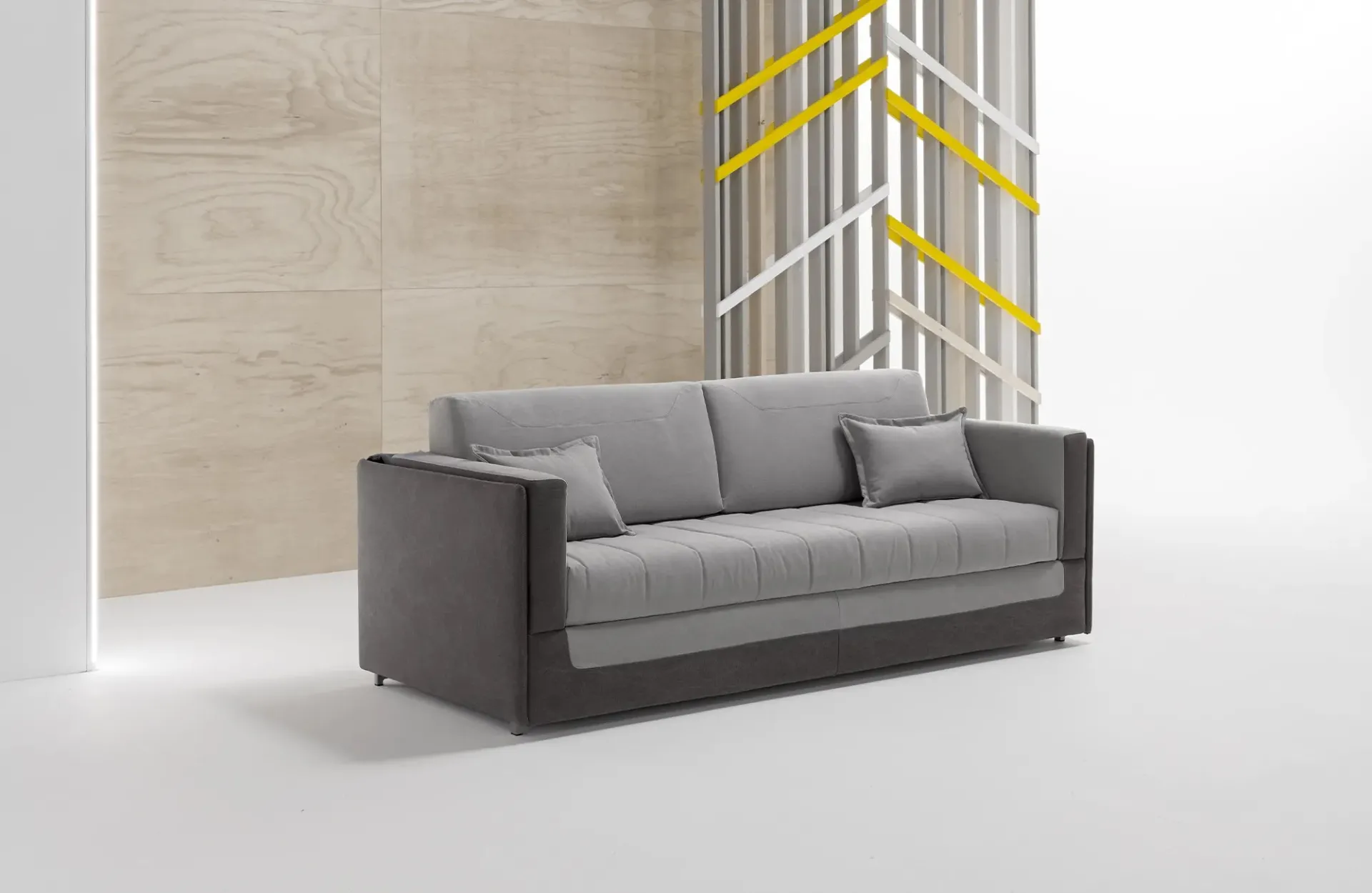 Divano letto a castello Coupé Dienne grigio con base scura davanti a una parete in legno