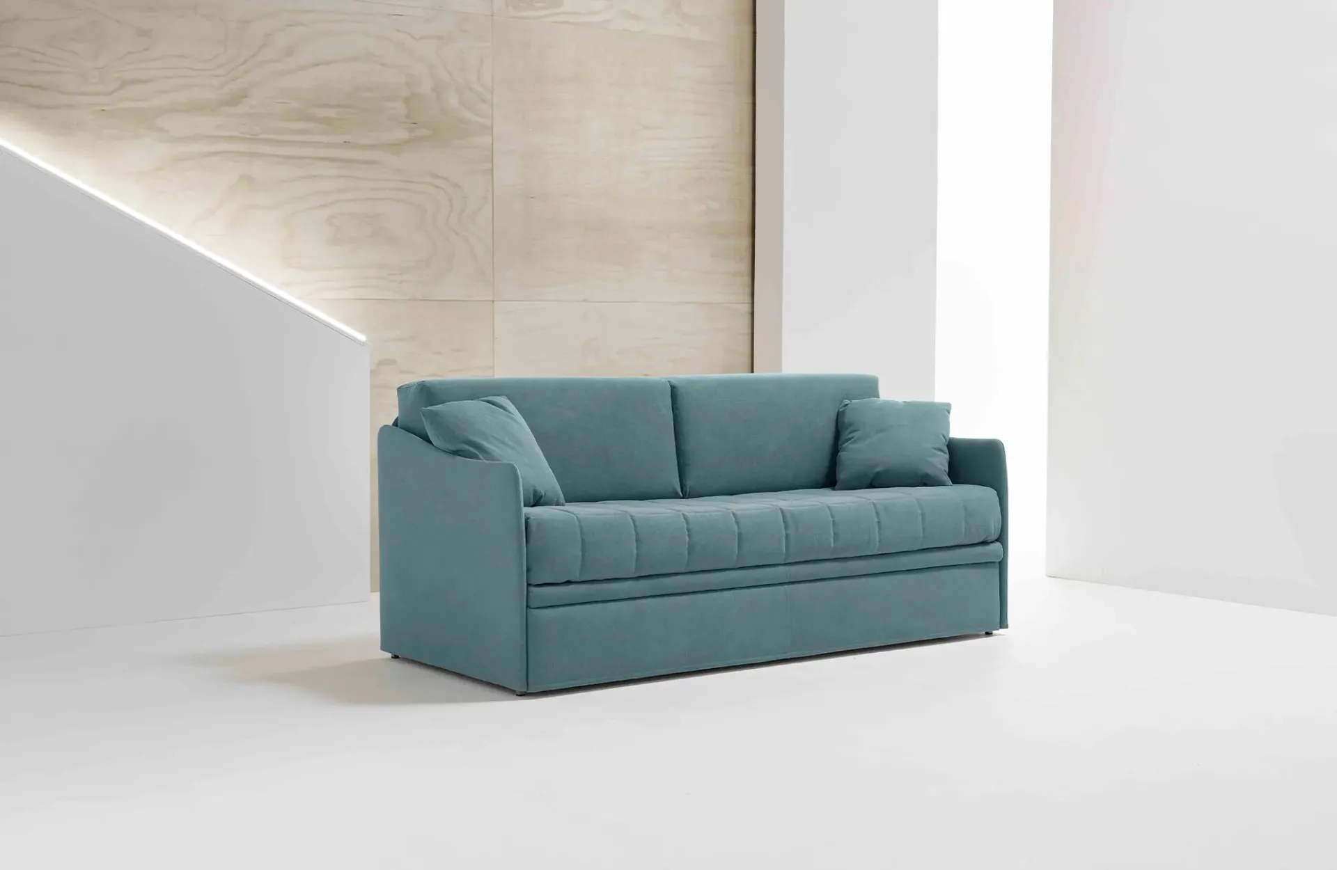 Divano letto Flo Dienne azzurro con seduta trapuntata davanti a una parete in legno chiaro