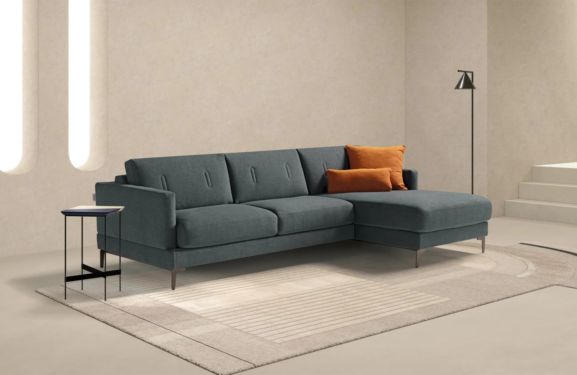Divano letto Evo Dienne verde petrolio con chaise longue e cuscino arancione in un soggiorno beige