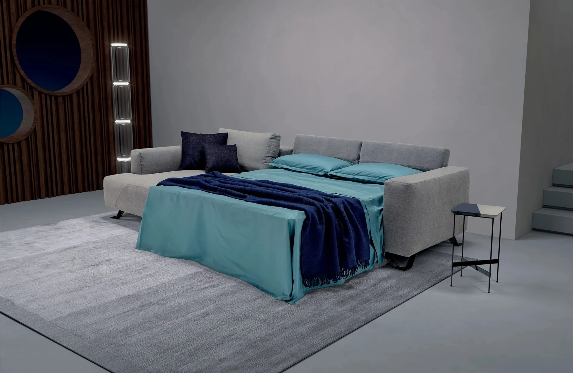 Divano letto Simple Dienne aperto con lenzuola azzurre accanto alla penisola