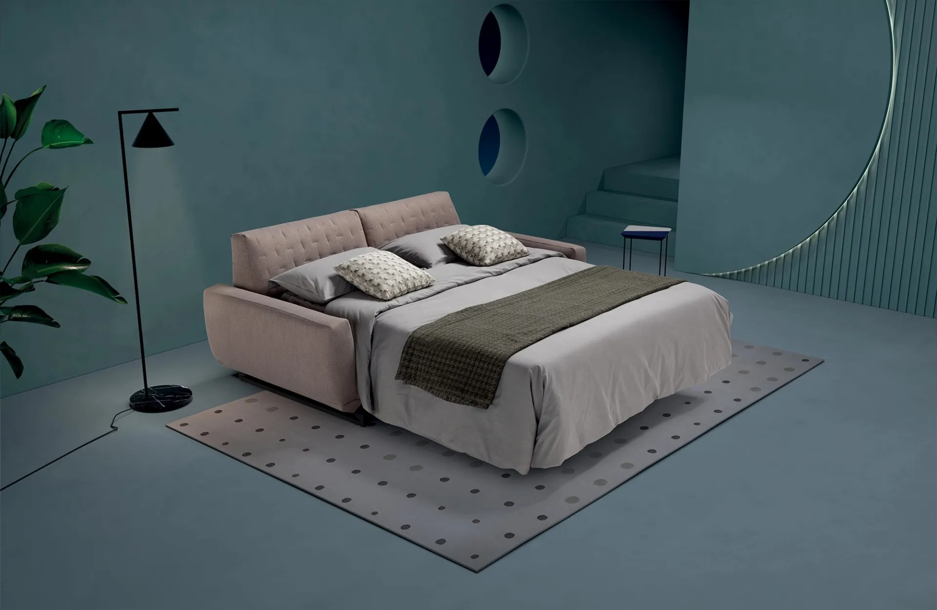 Divano letto Skin Dienne aperto con lenzuola grigie e coperta verde oliva