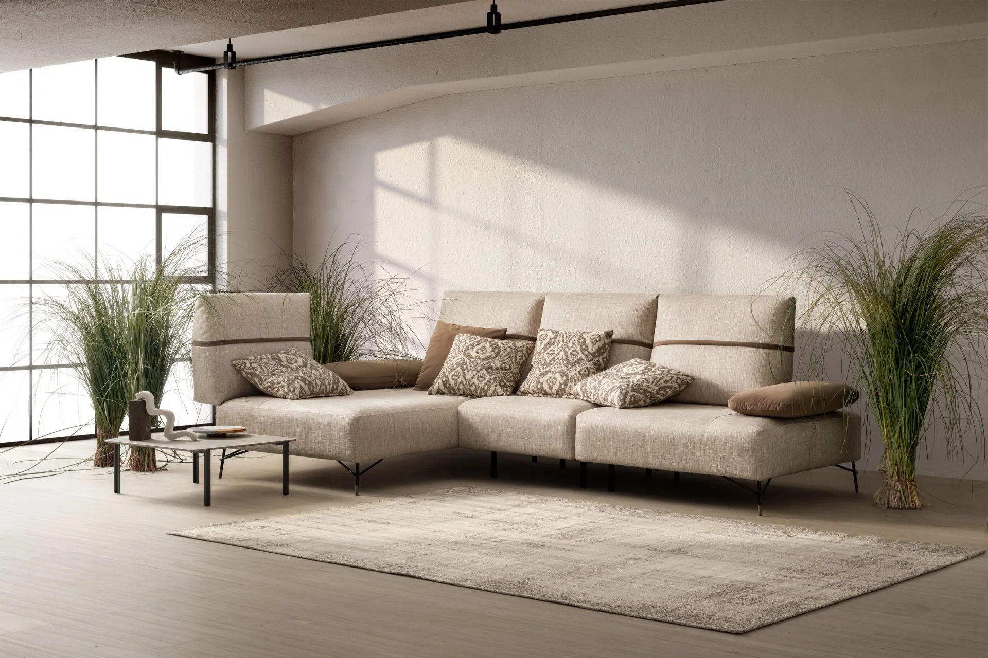 Divano Pull Samoa beige ad angolo con chaise longue e poggiatesta alzati, in un soggiorno con vetrata