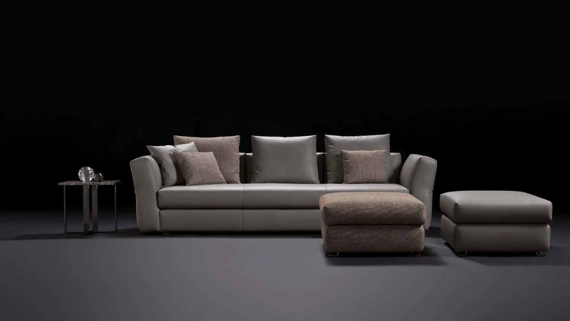 Divano Silverstone Rosini grigio con due pouf su fondo nero