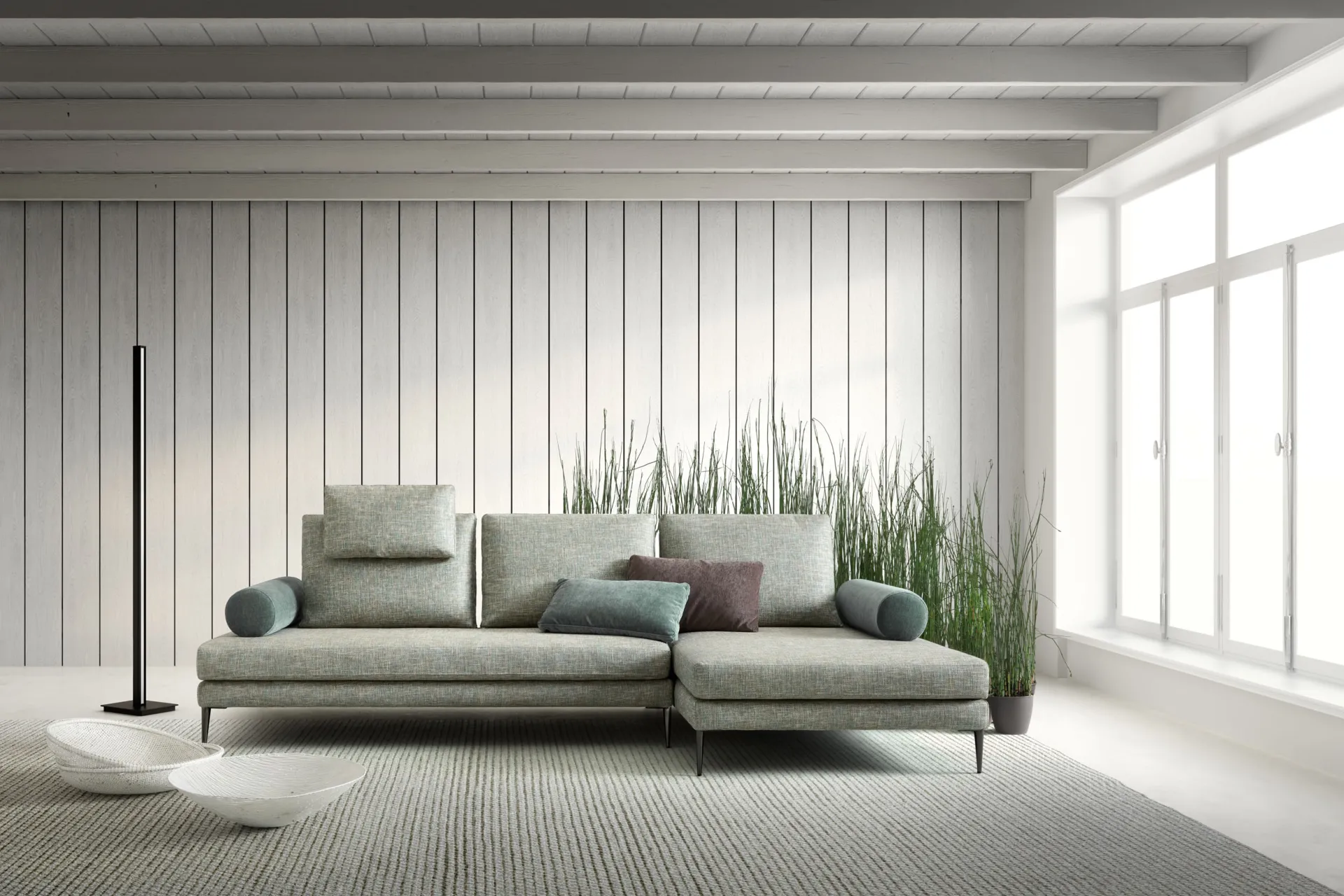 Divano Sound Samoa verde salvia con chaise longue e cuscini a rullo, davanti a una parete a doghe bianche