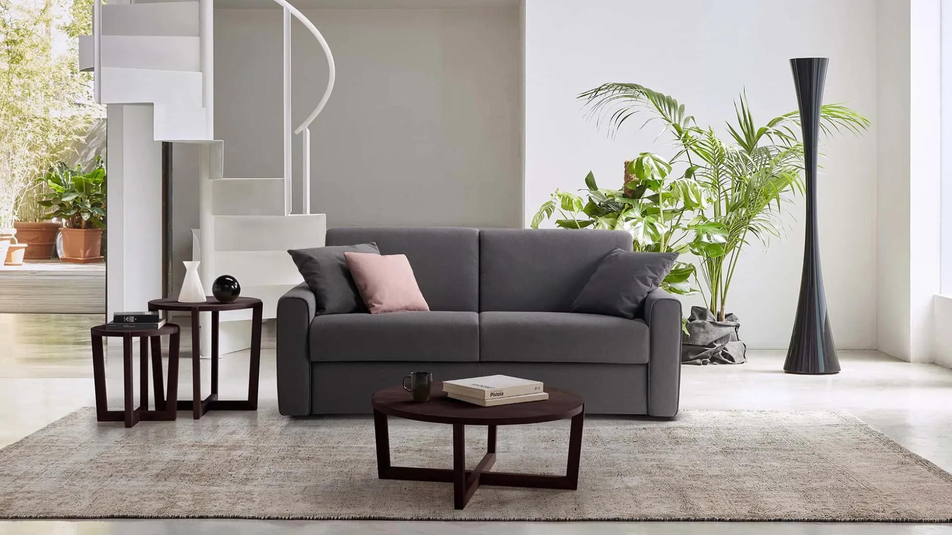 Divano letto Riva Rosini grigio con cuscino rosa e tavolino rotondo
