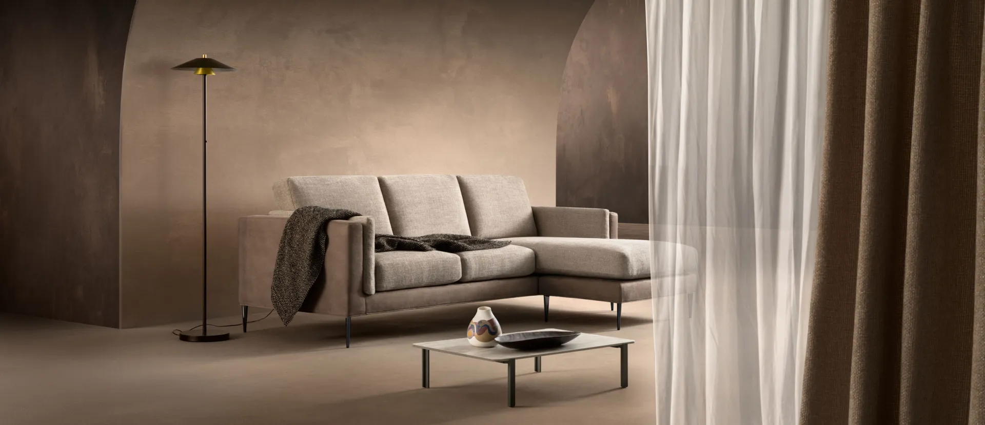 Divano Sheer Samoa con penisola fra tende color bronzo e lampada da terra