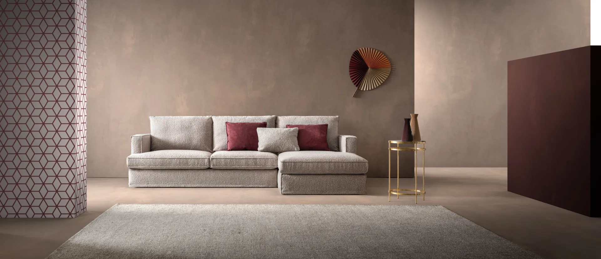 Divano Glammy Samoa chiaro con penisola e cuscini bordeaux su un tappeto grigio