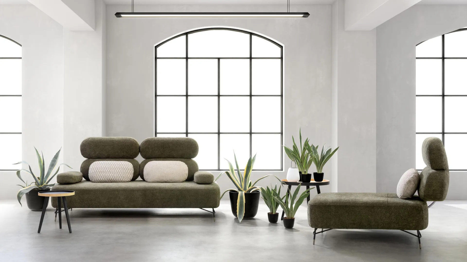 Divano Avalon Samoa verde oliva con cuscini chiari e chaise longue separata, in un loft con finestra ad arco