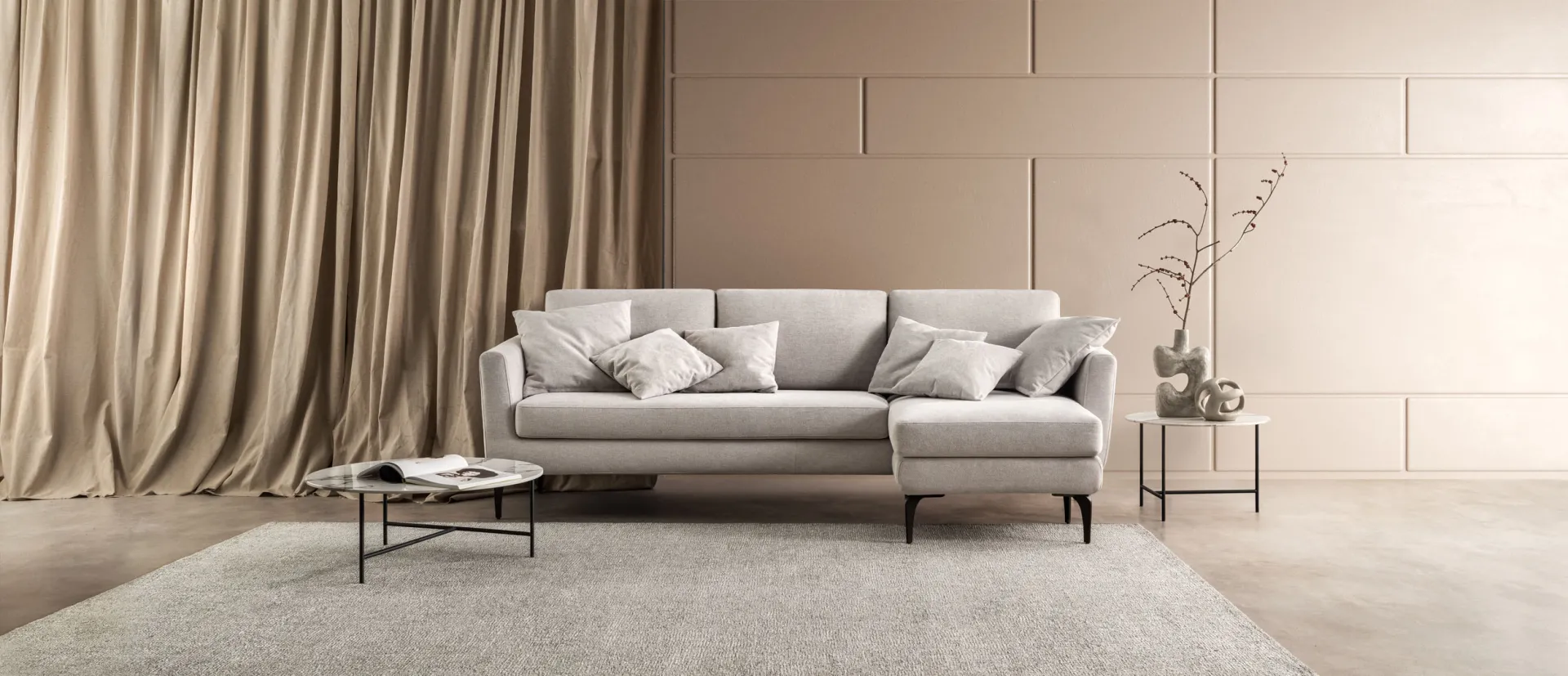 Divano Crisp Samoa chiaro con chaise longue su un tappeto, fra tende color sabbia