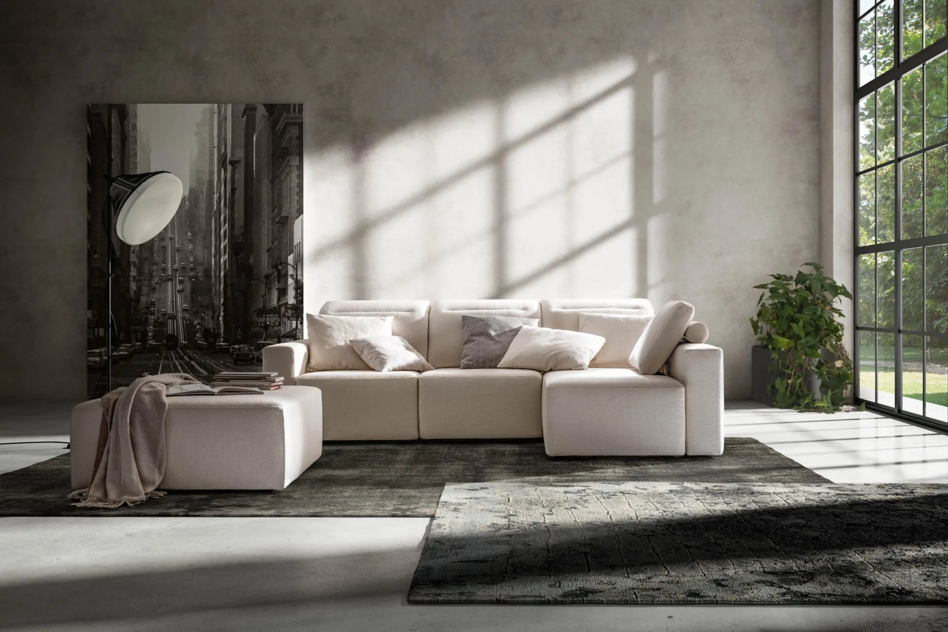 Divano Glide Samoa color panna con pouf, in un loft con grandi finestre