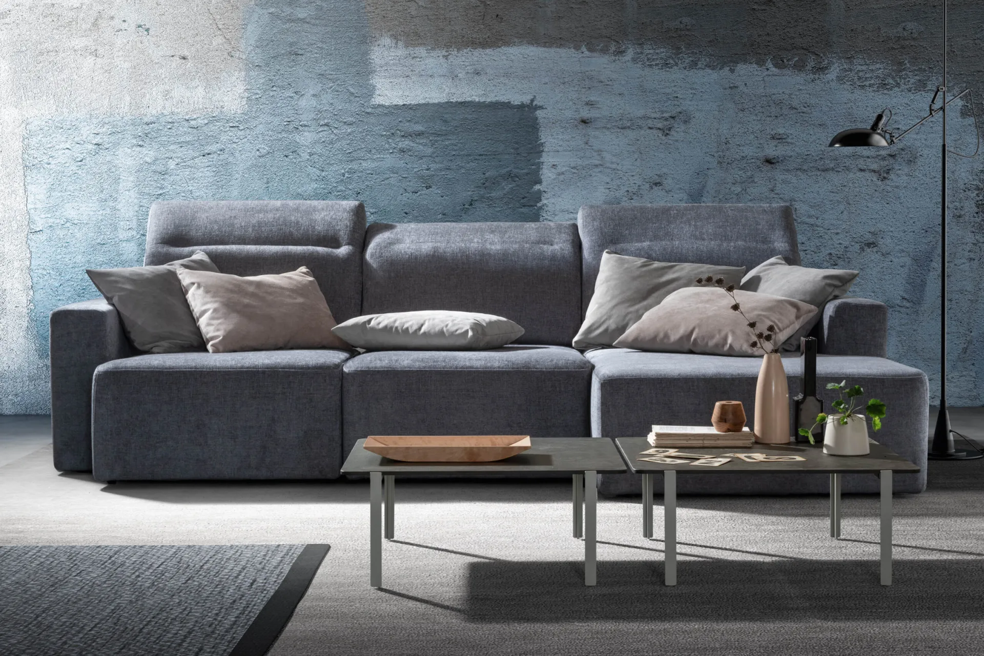 Divano Glide Samoa grigio azzurro con schienali reclinati, davanti a una parete dipinta
