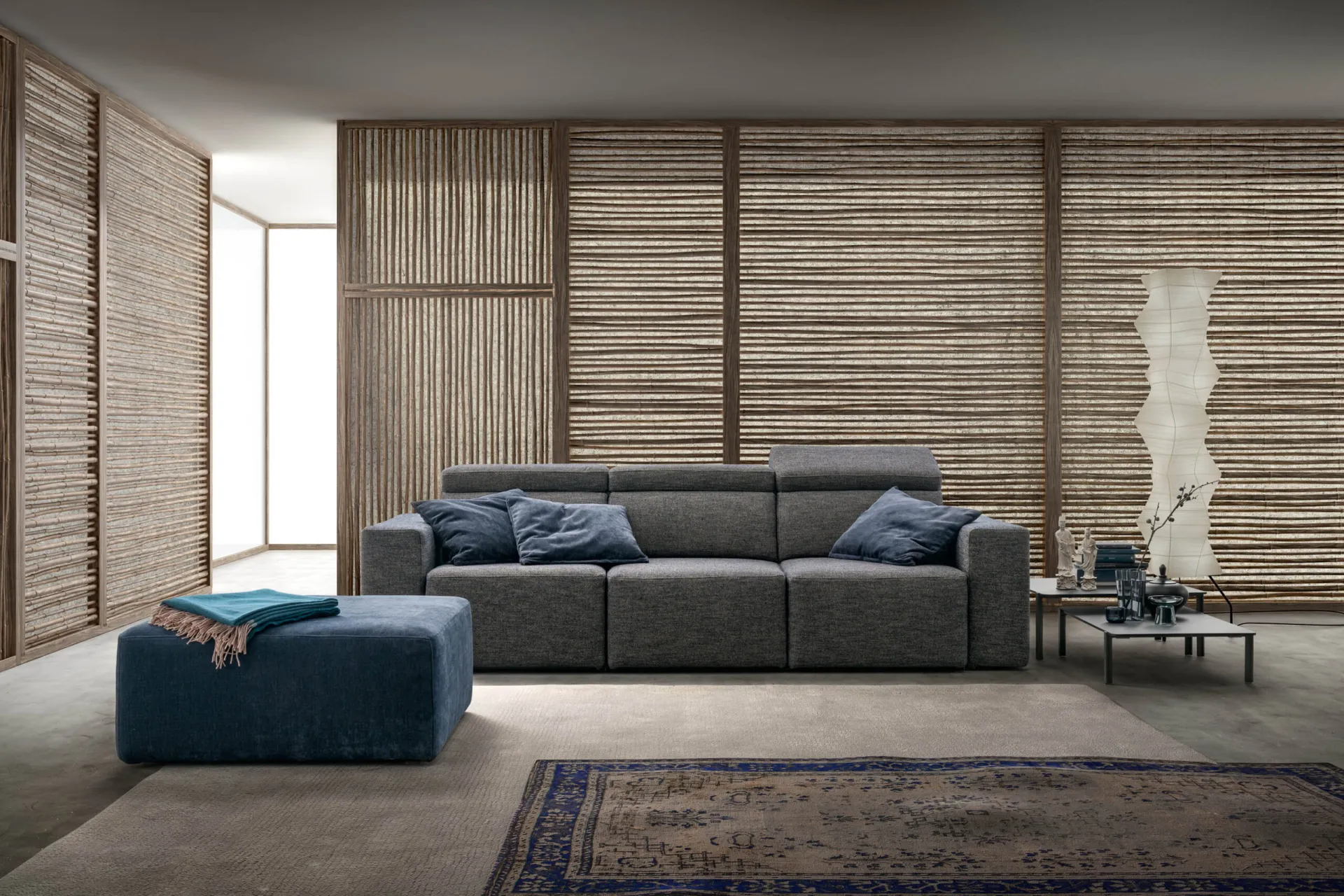Divano Best Samoa grigio con pouf blu, davanti a pannelli in fibra intrecciata