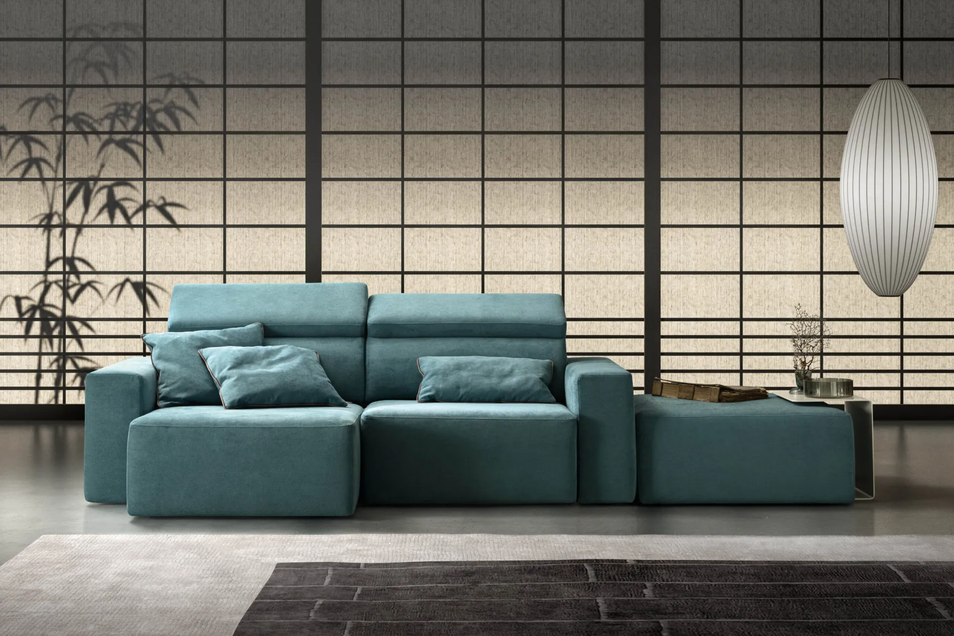 Divano Best Samoa ottanio con chaise longue e poggiatesta alzati, sotto una lampada a sfera