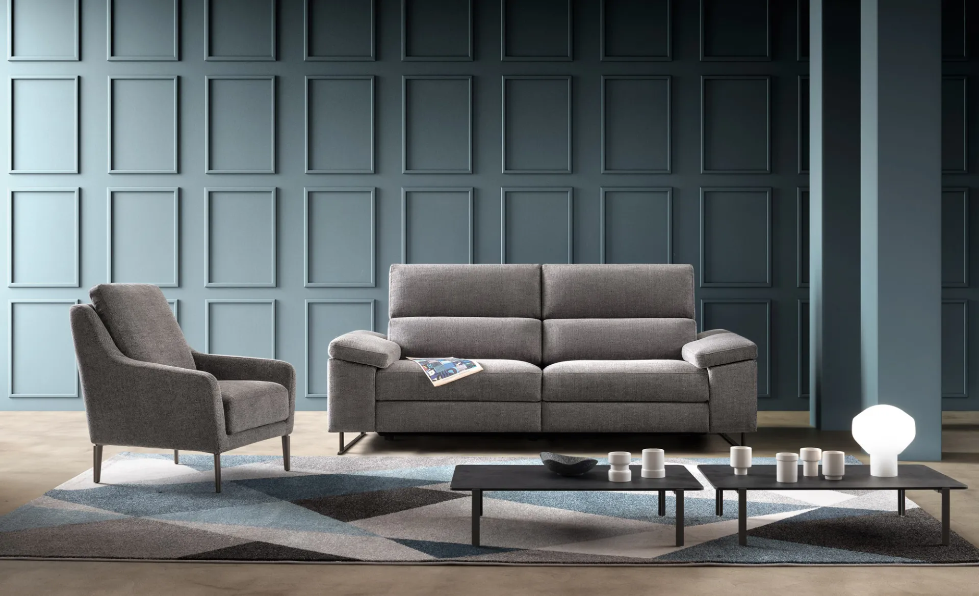 Divano Space Look Samoa grigio a tre posti accanto a una poltrona, davanti a pareti blu